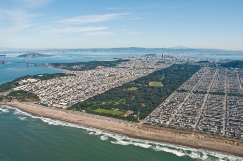 Aerial view of San Francisco, showcasing the city, coastline, and green spaces with the Golden Gate Bridge in the background.