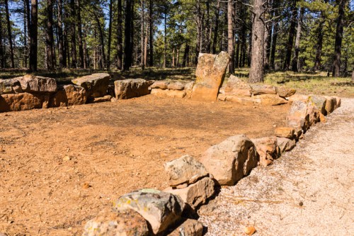 A cleared area surrounded by stones in a forest, with a large upright stone in the background.
