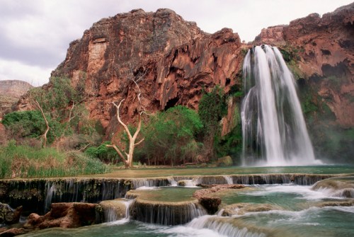 A serene waterfall cascades over rocky cliffs, surrounded by lush greenery and a tranquil pool below.