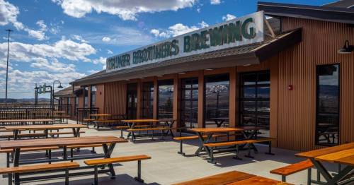 Exterior of a brewery with a sign, featuring outdoor seating and a clear blue sky with clouds.
