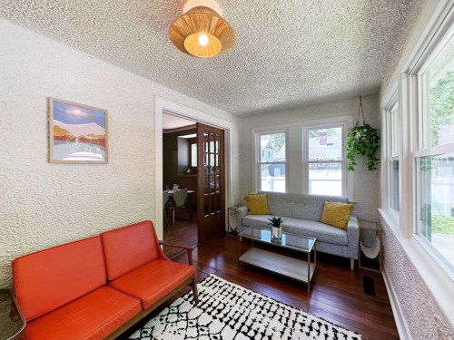 Cozy living room with orange couch, glass coffee table, and large windows, featuring textured walls and a pendant light.