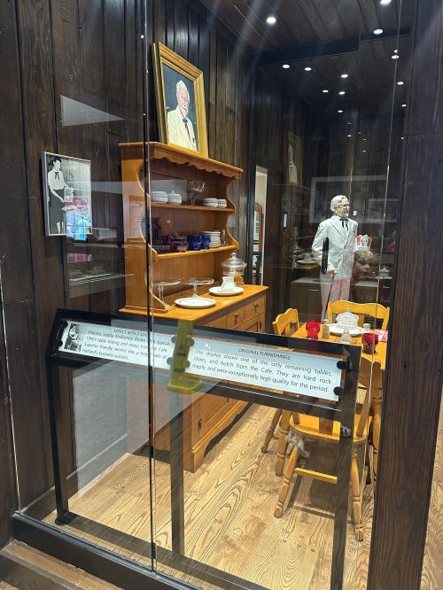 Display case featuring a vintage dining set, wooden furniture, and a portrait, showcasing historical artifacts.