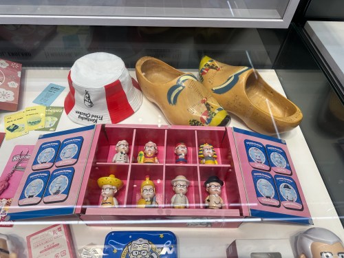 Display case featuring collectible figurines, wooden clogs, and a KFC bucket, all arranged neatly.