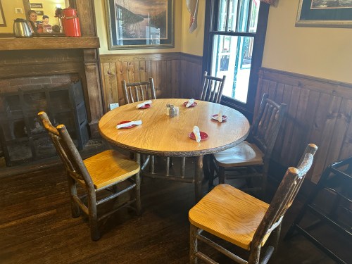 A wooden round table set for four, with napkins, in a cozy rustic dining area.
