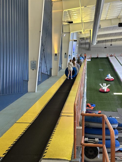 A conveyor belt leading up a slope, with people preparing to slide down on inflatable tubes.