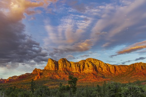 Sunset over red rock formations with dramatic clouds in the sky, creating a vibrant and colorful landscape.