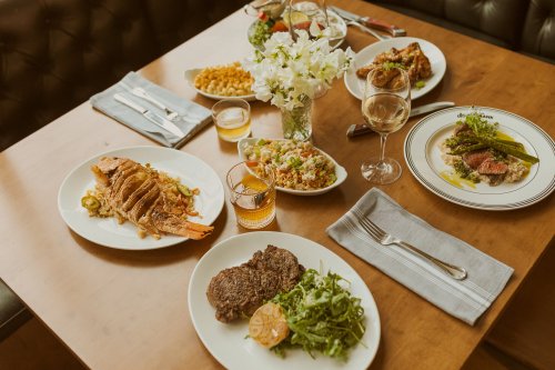 A dining table set with various gourmet dishes, including fish, steak, sides, and drinks, surrounded by elegant decor.