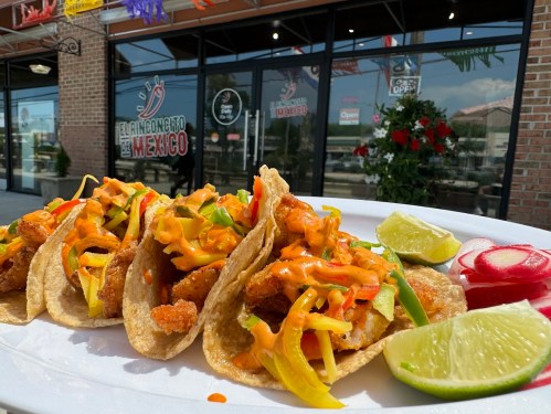 A plate of tacos filled with shrimp, topped with vegetables and sauce, served with lime and radish, outside a restaurant.