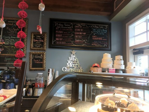 A cozy café interior with a chalkboard menu, festive decorations, and a display case of desserts.