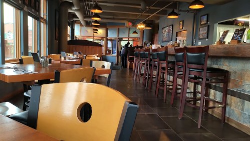 Interior of a restaurant featuring wooden tables, high chairs, and large windows with warm lighting.
