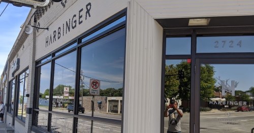 Exterior view of Harbinger building with large windows reflecting the street and a person taking a photo.