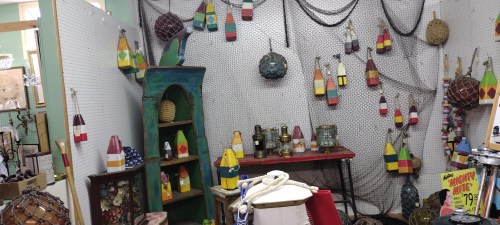 A colorful display of fishing buoys and nautical decor in a vintage shop, with nets and various artifacts.