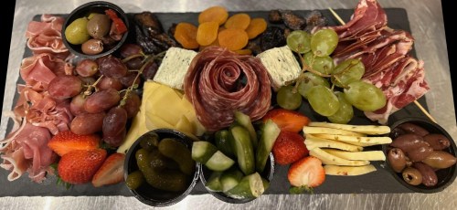 A charcuterie board featuring meats, cheeses, fruits, and pickles arranged on a slate platter.
