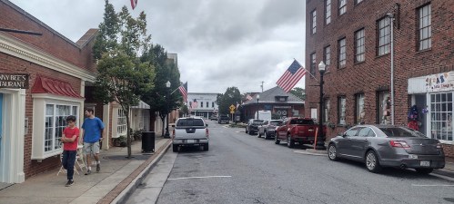 A quiet street scene with people walking, American flags, and brick buildings lining the road.