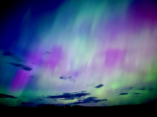 Vibrant aurora borealis lights up the night sky with shades of green, purple, and blue, amidst scattered clouds.