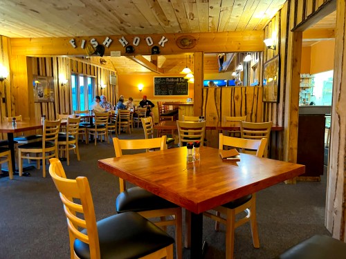 Cozy restaurant interior with wooden decor, empty tables, and patrons in the background enjoying their meals.