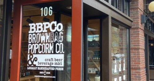 Exterior of BBP Co. Brown Bag Popcorn Co. featuring a wooden bench and nearby outdoor seating area.