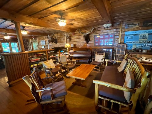 Cozy log cabin interior with wooden furniture, a piano, and rustic decor, creating a warm, inviting atmosphere.