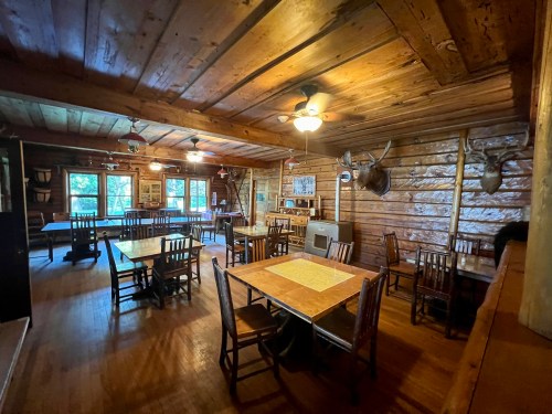 Cozy wooden dining room with tables, chairs, and rustic decor, featuring a mounted deer head on the wall.