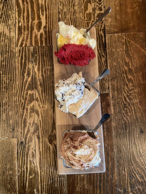 Three scoops of ice cream in bowls on a wooden board: red sorbet, cookies and cream, and cinnamon swirl.