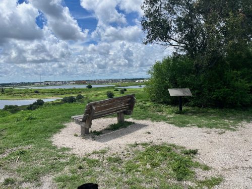 A wooden bench overlooks a scenic view of a river and green landscape under a partly cloudy sky.