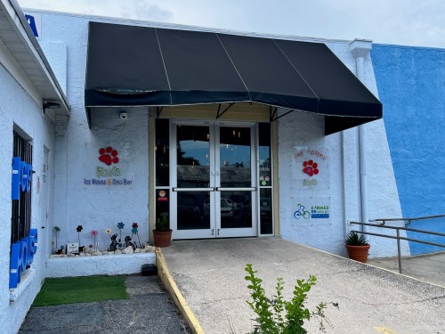 Entrance of a pet house and bar with a black awning, blue walls, and decorative paw prints on the exterior.