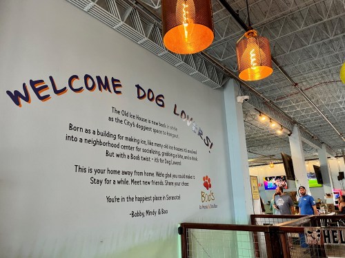 Interior of a dog-friendly venue with a welcoming wall sign for dog lovers, featuring a friendly message and people in the background.