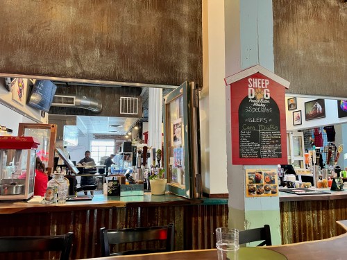 Interior of a cozy restaurant with a bar, menu board, and patrons in the background. Warm, inviting atmosphere.