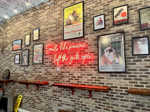 A brick wall adorned with vintage posters and a neon sign that reads, "Smile like someone left the gate open."
