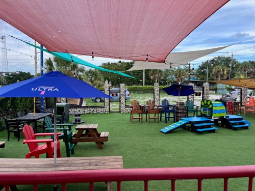 Outdoor seating area with colorful chairs, umbrellas, and a grassy surface, surrounded by decorative elements.