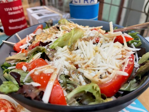 A close-up of a fresh salad with mixed greens, sliced tomatoes, and shredded cheese, drizzled with dressing.