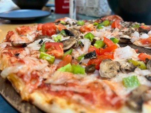 A close-up of a pizza topped with tomatoes, green peppers, onions, and mushrooms on a wooden surface.