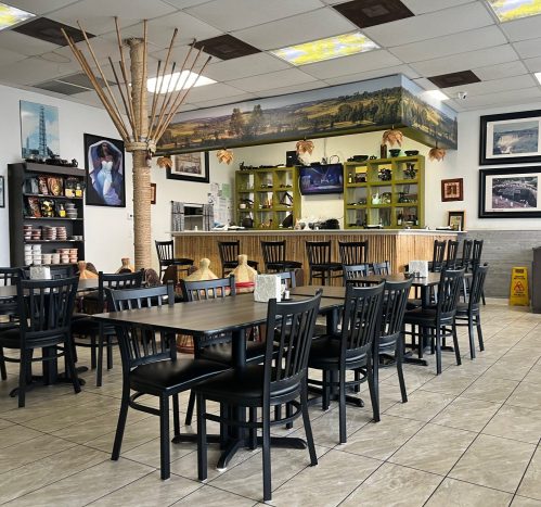 Interior of a restaurant featuring black tables and chairs, a wooden counter, and decorative artwork on the walls.