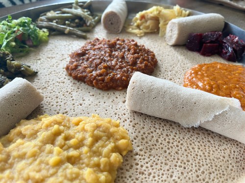 A platter of Ethiopian food featuring injera, lentils, spicy stew, and various vegetable sides.