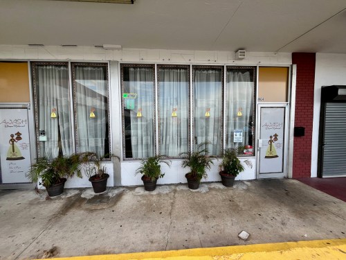 Exterior of a storefront with large windows, potted plants, and decorative signage featuring a character.