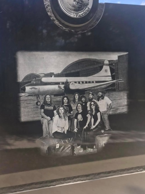 A black and white photo of a group of people with luggage in front of an airplane and hangar.