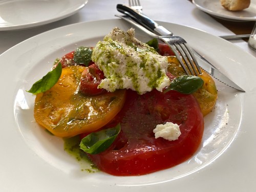 A plate of colorful sliced tomatoes topped with fresh basil and creamy cheese, drizzled with olive oil and seasoning.