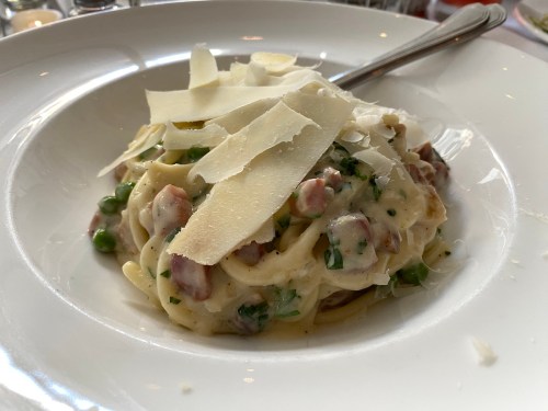 A plate of creamy pasta with peas, pancetta, and shaved Parmesan cheese on top.
