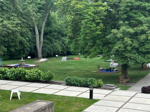 A green park with various sculptures and installations, surrounded by trees and a paved walkway.