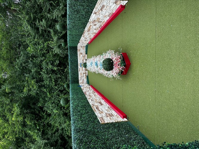 A landscaped garden featuring a central floral arrangement surrounded by green hedges and stone walls.