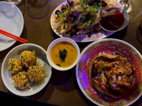 A table with three dishes: golden dumplings, a bowl of soup, and a flaky pastry topped with herbs, alongside chopsticks.