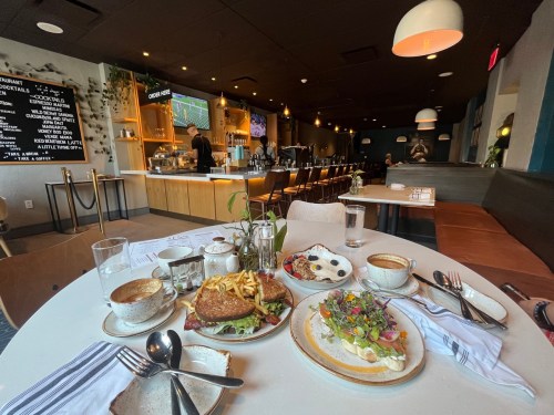A cozy restaurant interior with a table set for brunch, featuring various dishes and drinks, and a bar in the background.