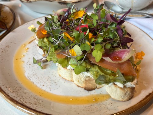 A beautifully plated avocado toast topped with microgreens, edible flowers, and a drizzle of honey on a rustic plate.