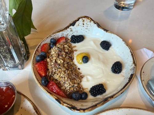 A bowl of yogurt topped with granola, strawberries, blueberries, and blackberries, garnished with a yellow fruit.