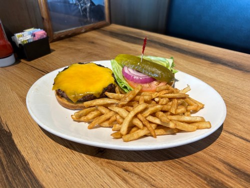 A plate with a cheeseburger topped with lettuce, onion, and pickle, served with a side of crispy fries.