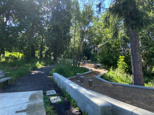 A serene park path surrounded by trees, with benches and a gravel area, inviting visitors to explore nature.