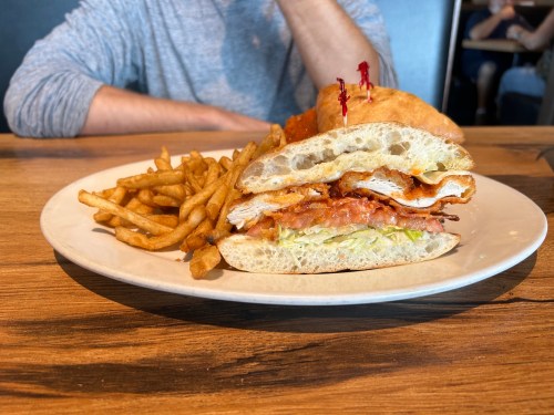 A close-up of a sandwich with fried chicken, lettuce, and bacon, served with a side of crispy French fries.