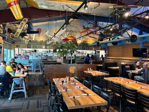 A vibrant restaurant interior featuring wooden tables, airplane decor, and diners enjoying their meals.