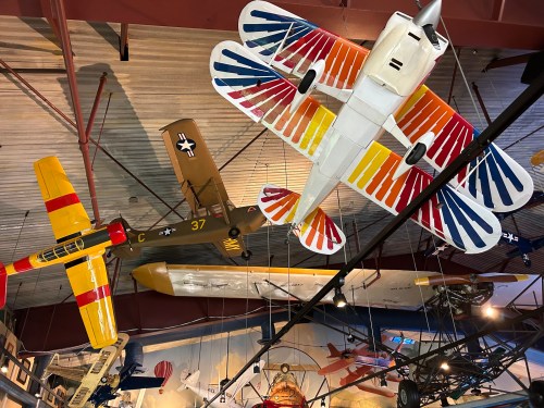 Colorful model airplanes hanging from the ceiling in a museum, showcasing various designs and styles.
