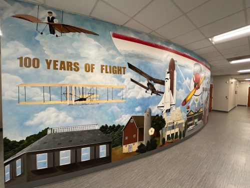 Mural celebrating 100 years of flight, featuring historic aircraft and a vibrant sky backdrop.